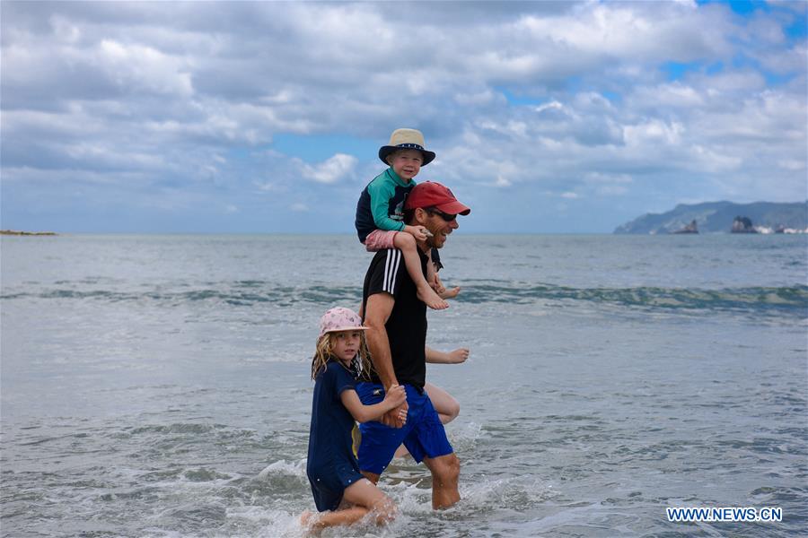 Tourists wade through waves via tide path between Whangamata beach