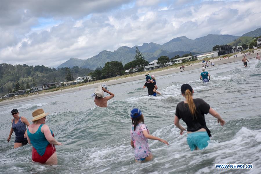Tourists wade through waves via tide path between Whangamata beach