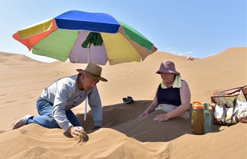 Tourists experience sand therapy in Kum Tag Desert of Xinjiang