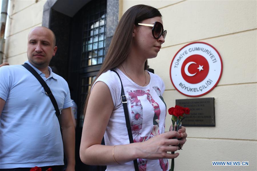 A woman stands with a placard reading 'No terrorism in a modern world' as people pass by to lay flowers in front of Turkish embassy in Russia in Moscow, Russia, on June 29, 2016. 