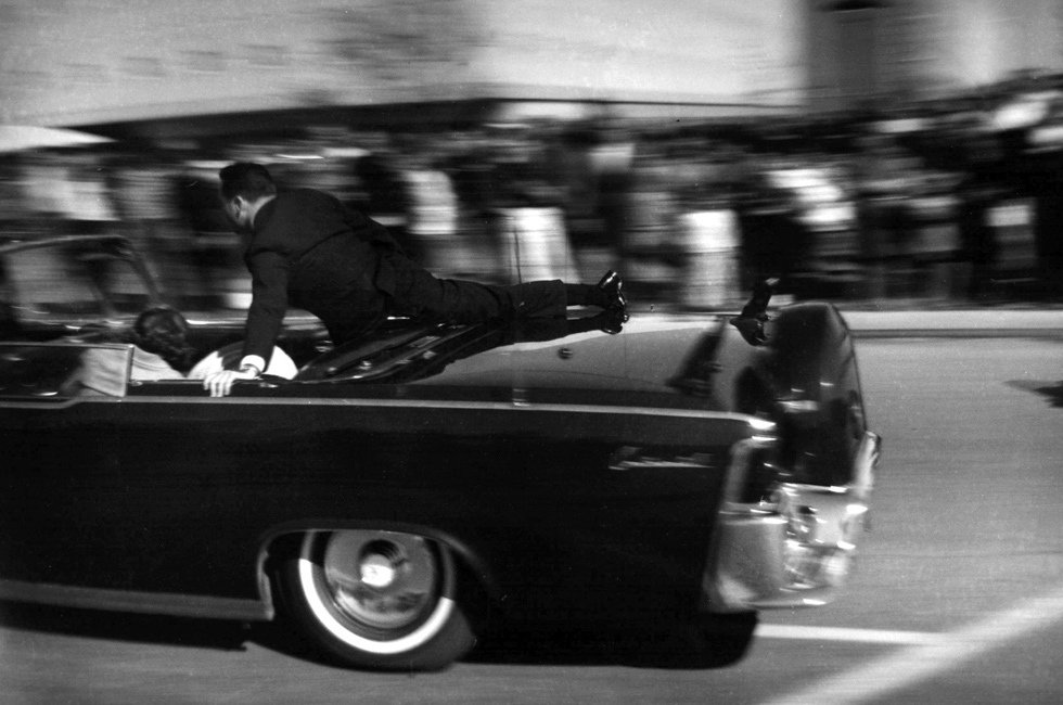 8.1963年11月22日12：30左右，肯尼迪总统在被枪击后倒在了车后座上，第一夫人杰奎琳-肯尼迪俯身在总统边，特工克林特-希尔试图将她推回座位上，以防其掉出车外。