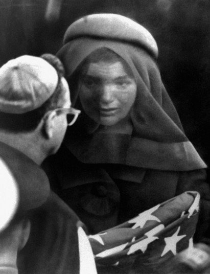 23.1963年11月25日，在阿灵顿国家公墓内，总统下葬后，其遗孀杰奎琳-肯尼迪手拿覆盖丈夫棺柩的国旗。