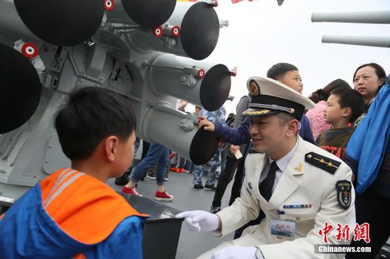 4月23日，中国人民解放军海军成立67周年纪念日，挂满旗的导弹驱逐舰哈尔滨舰停靠在青岛某军港码头向当地市民开放。与此同时，在旅顺某军港码头，导弹护卫舰葫芦岛舰也悬挂着象征节日最高礼仪的满旗对外开放。图为哈尔滨舰军官为小朋友讲解装备。