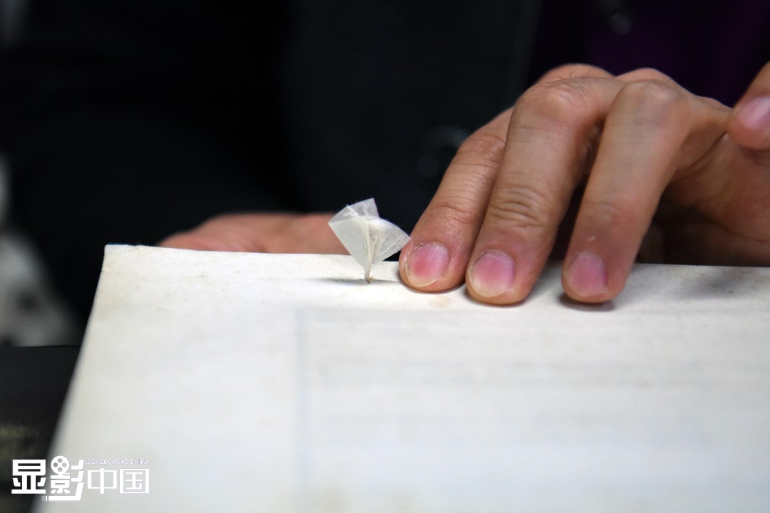 4月20日，季玉方给修复的古籍上纸捻，小小的纸捻能将理齐的古籍散页牢牢地固定住。