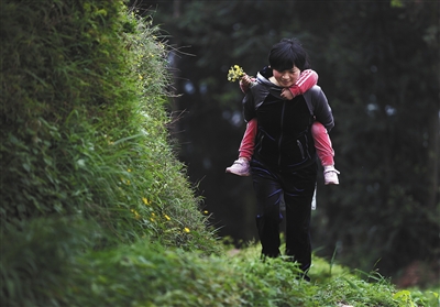 居仁中学的王蕾老师,背着女儿走在去家访的山路上。