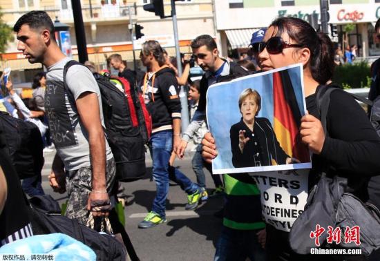 布达佩斯街头，难民手持默克尔照片徒步前往匈奥边境。德国和匈牙利表示，最新帮助安置难民措施仅仅是为了避免危机，不能成为长期先例。