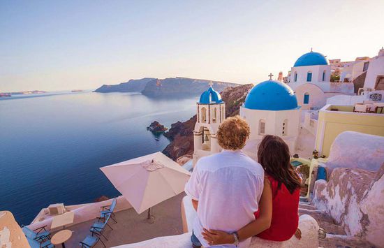 度假宣传手册上显示，一对夫妇正坐在希腊圣托里尼岛（Santorini）蔚蓝的爱琴海边欣赏落日美景。(网页截图)