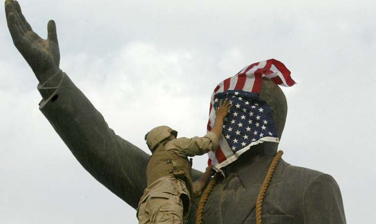 2003年4月，一名美军士兵爬上伊拉克前总统萨达姆的塑像，将美国国旗盖在塑像的脸上。