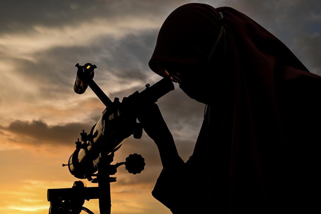 a woman via a telescope observes the new moon that signals the